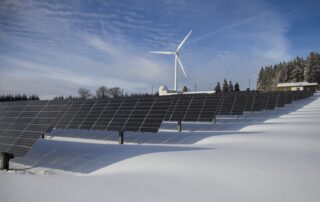 Solar panels on snow with windmill under clear day sky as a way of implementing sustainable business practices.