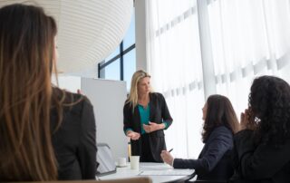 Four female leaders gathered around a meeting table having a discussion.