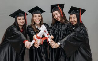 Four successful female college graduates holding diplomas and smiling.