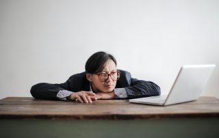 Bored formal man watching laptop at desk working on overcoming procrastination