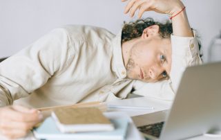 Overworked employee lying in front of laptop, appearing exhausted and needs to overcome burnout.